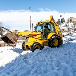 Yellow excavator removing snow in the city.